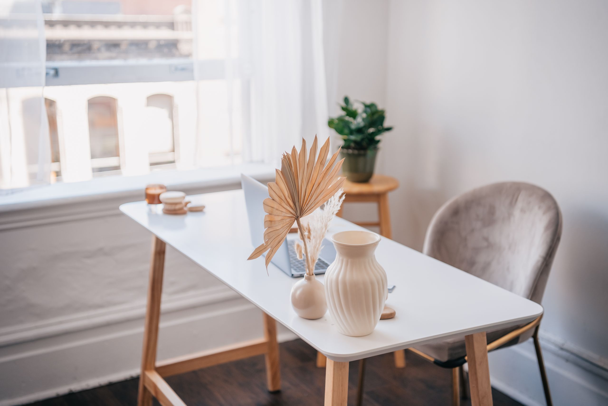 Modern office desk with laptop and minimalist decor near a window.